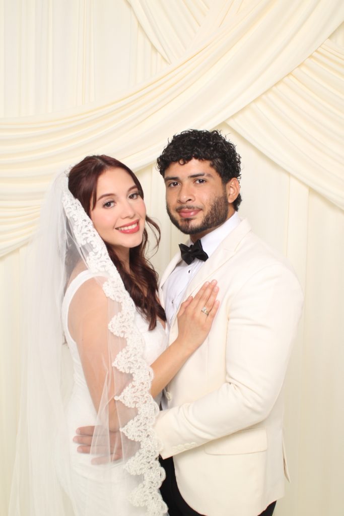 Bride and groom smiling together in front of an ivory drape backdrop