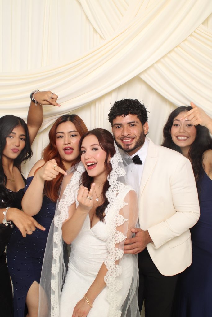 Bride and groom posing playfully with friends in front of an ivory drape backdrop
