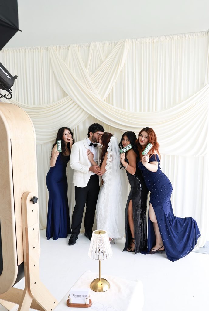 Guests posing at the Memento mirror photo booth with an ivory drape backdrop