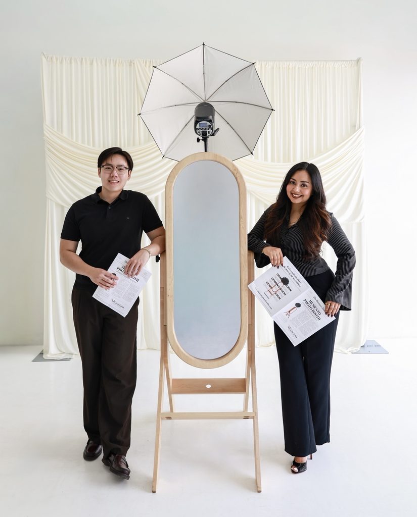 The Memento Photo Booth team standing beside the mirror booth, holding printed photo strips